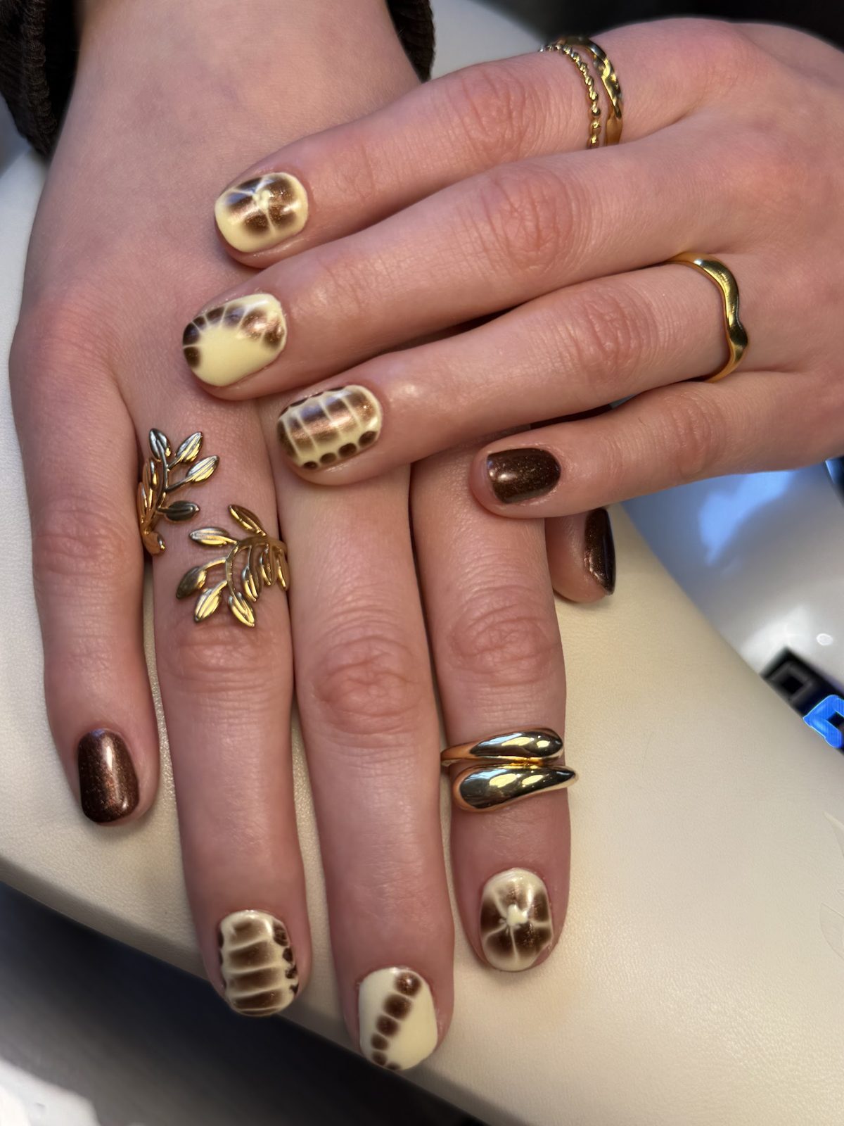 Handen met biab in crème en bruine dierenprint, met twee nagels in bruine chrome, op het kussen in de salon