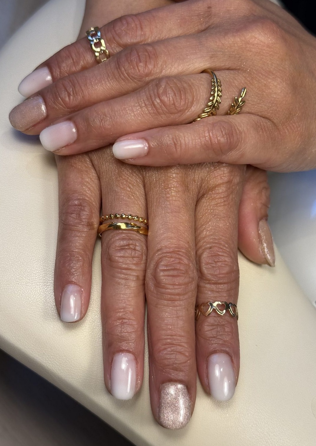 Twee handen met melkwitte en zachtroze nagels en gouden ringen