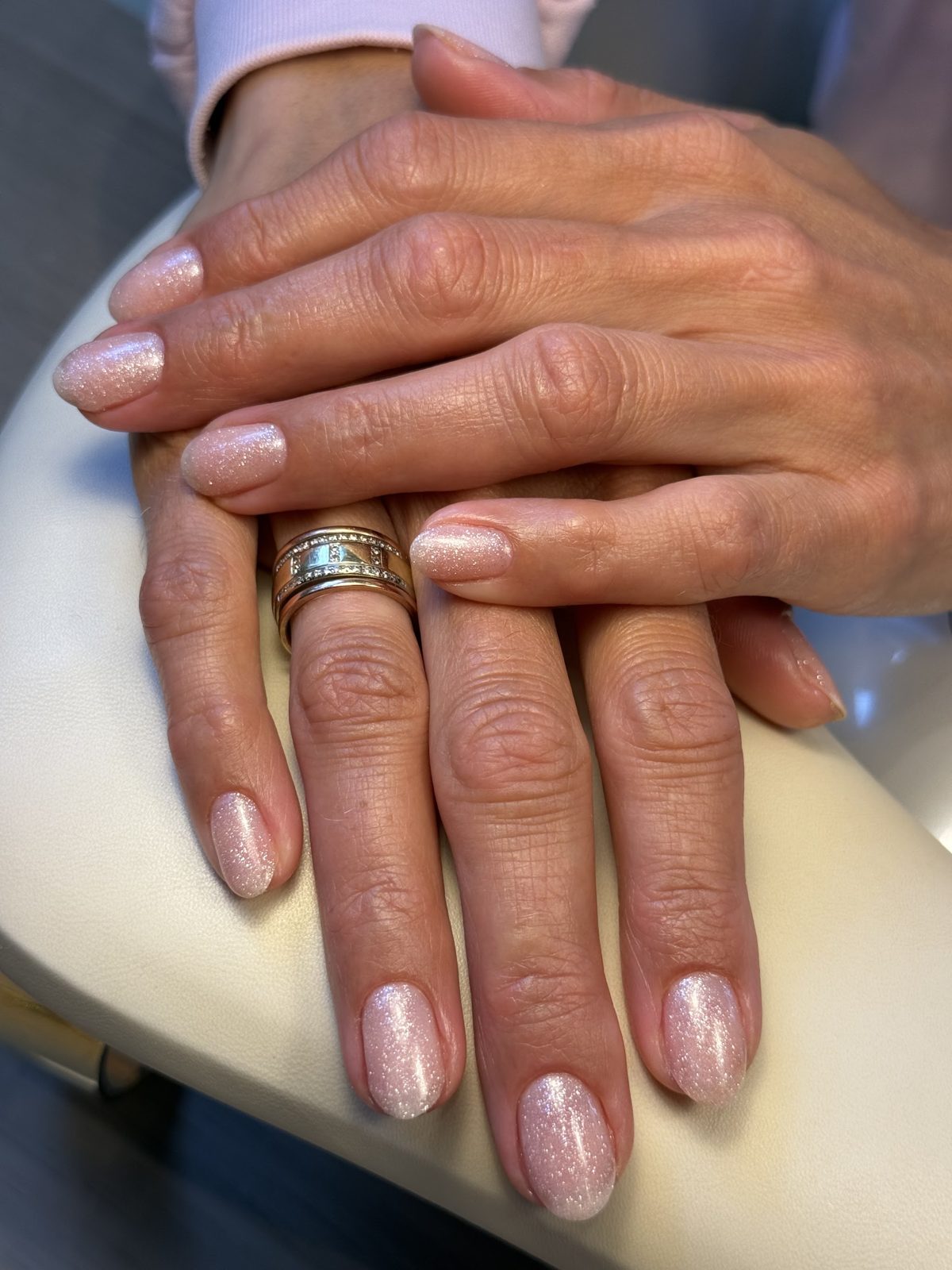Twee handen met roze glanzende nagels op het crème kussen in de salon